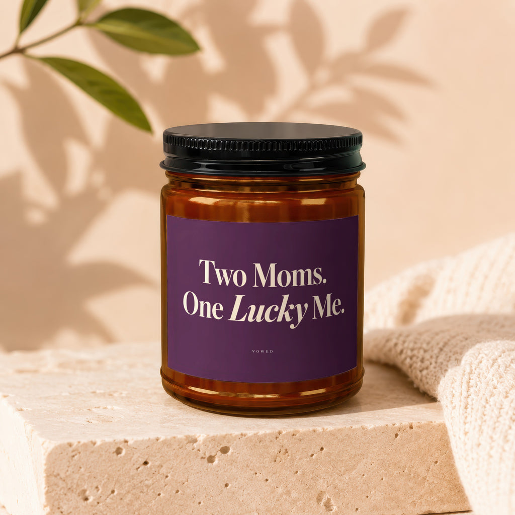 Amber jar candle with purple label reading "Two Moms. One Lucky Me."