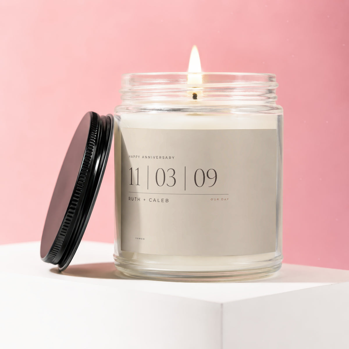Jar candle with lit wick, black lid, and custom label for Ruth + Caleb anniversary.