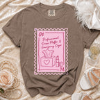 Brown t-shirt with a pink postage stamp graphic reading "0¢ Professional Dress Fluffer & Emergency Cryer".