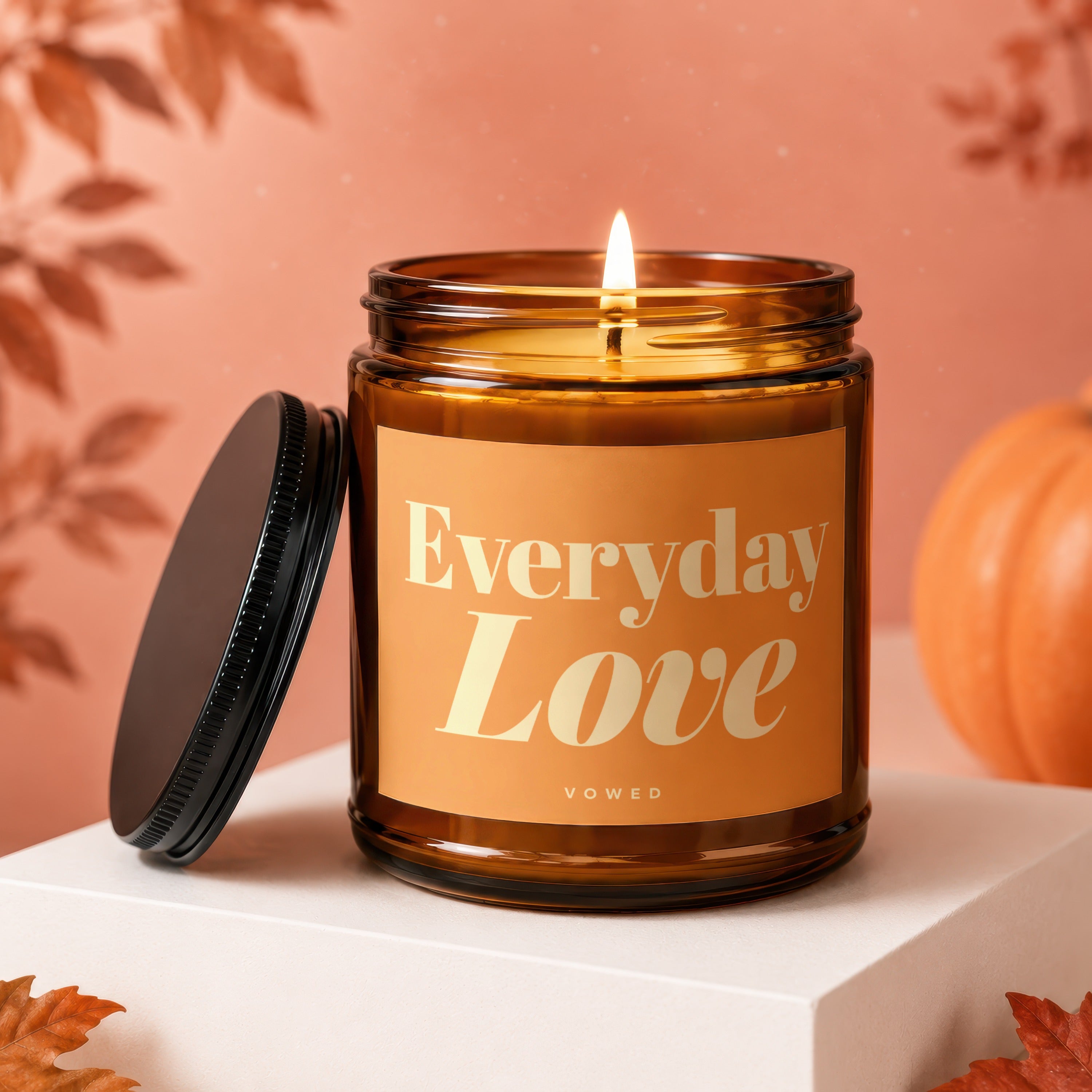 Lit amber candle with "Everyday Love" text, lid off, autumn theme.