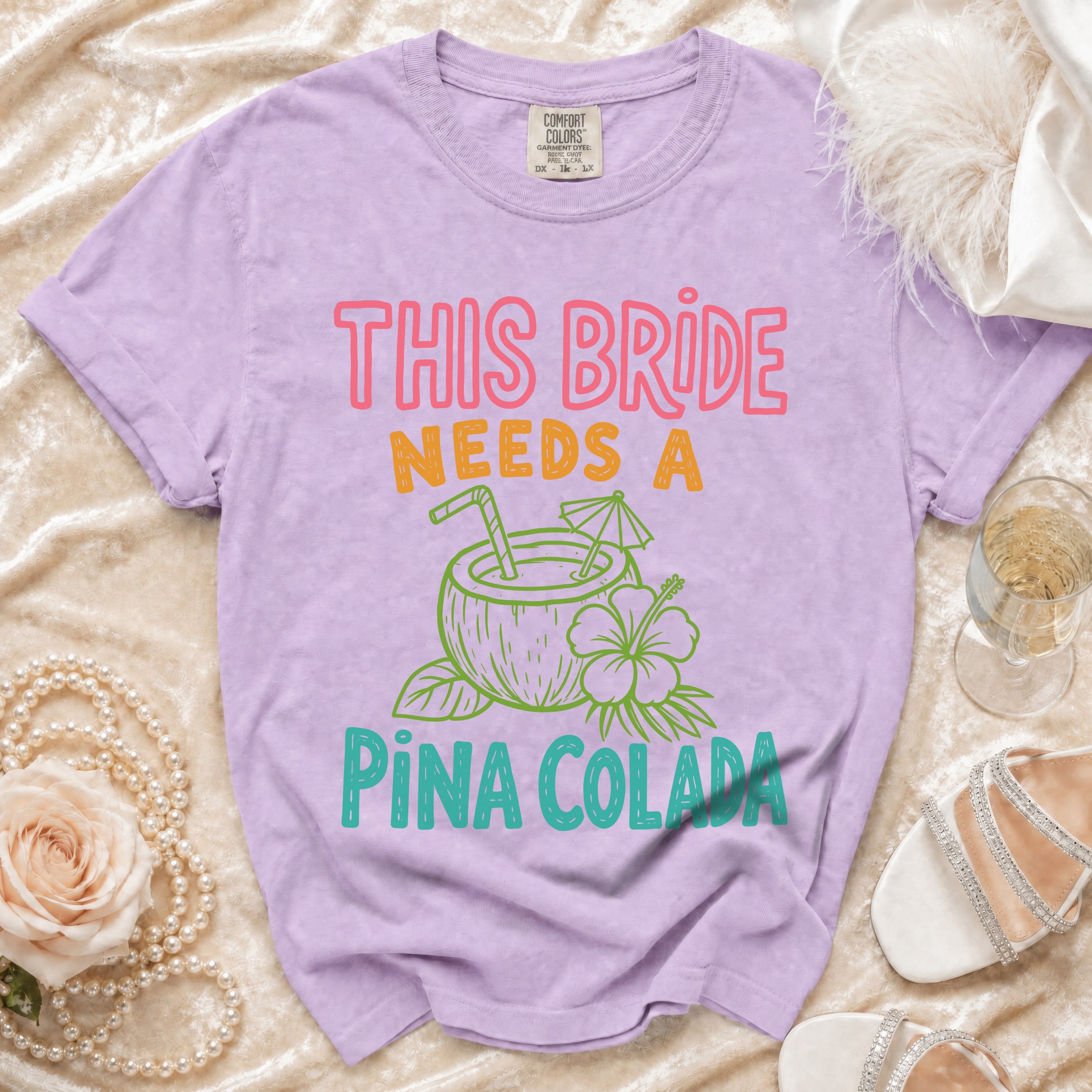 Purple t-shirt with "THIS BRIDE NEEDS A PINA COLADA" graphic and coconut drink.