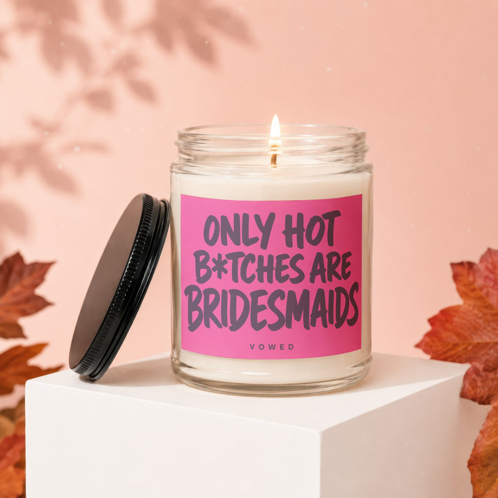 Glass candle with a burning wick and a pink label that reads "ONLY HOT B*TCHES ARE BRIDESMAIDS VOWED".