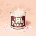Candle with "Hexes. Hairspray. Hysteria." text on label, surrounded by pink petals.