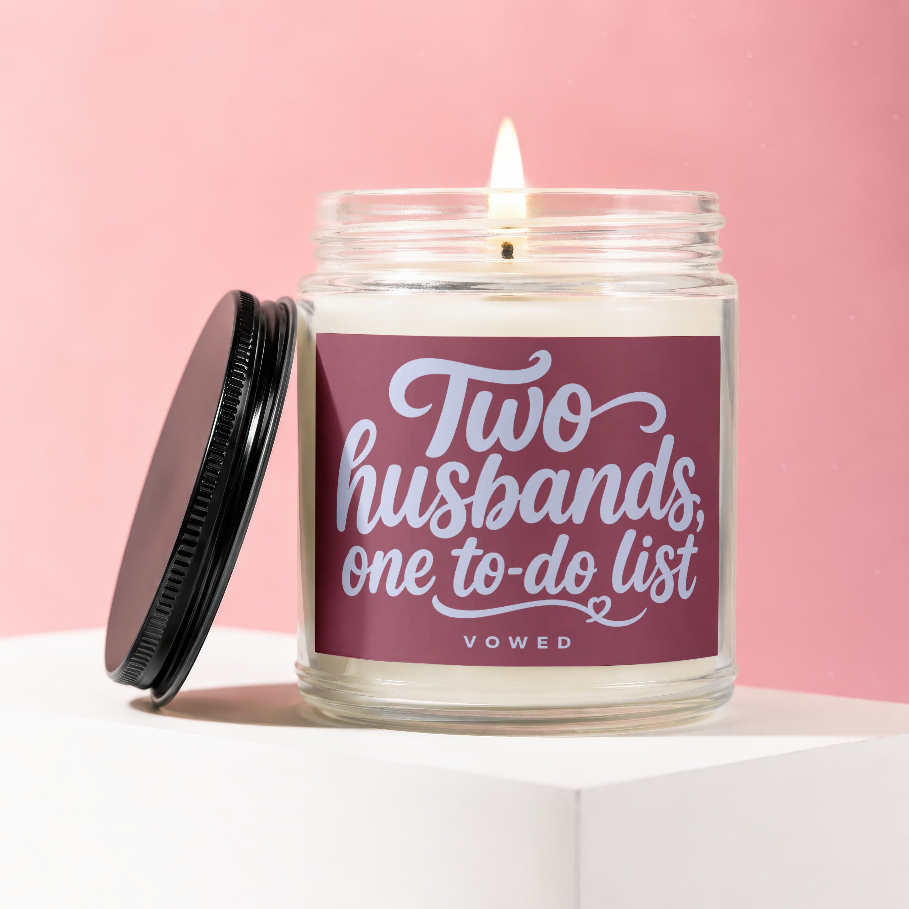 Candle with text "Two husbands, one to-do list VOWED" on a pink background.