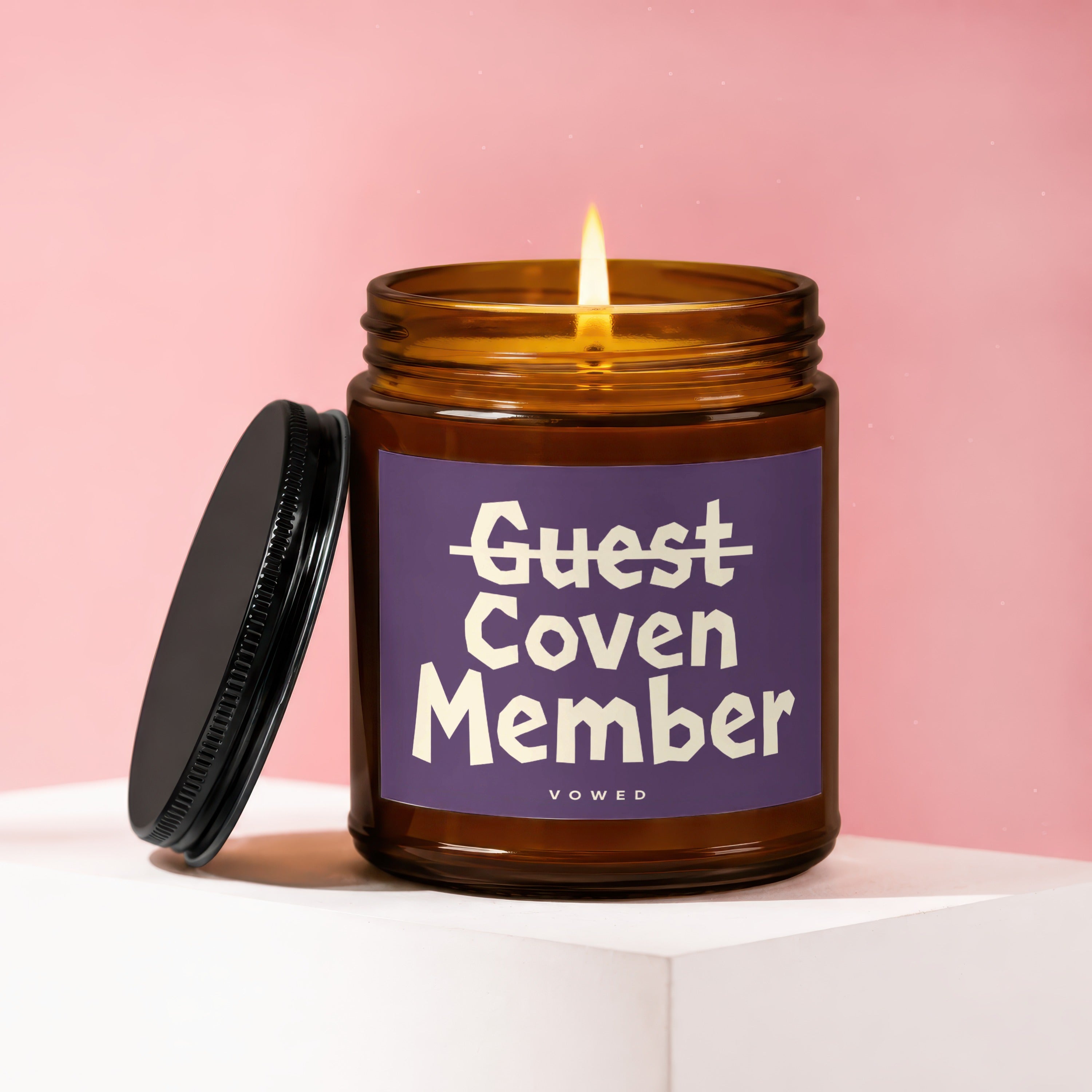 Amber jar candle with lit flame and lid, labeled "Guest Coven Member Vowed".