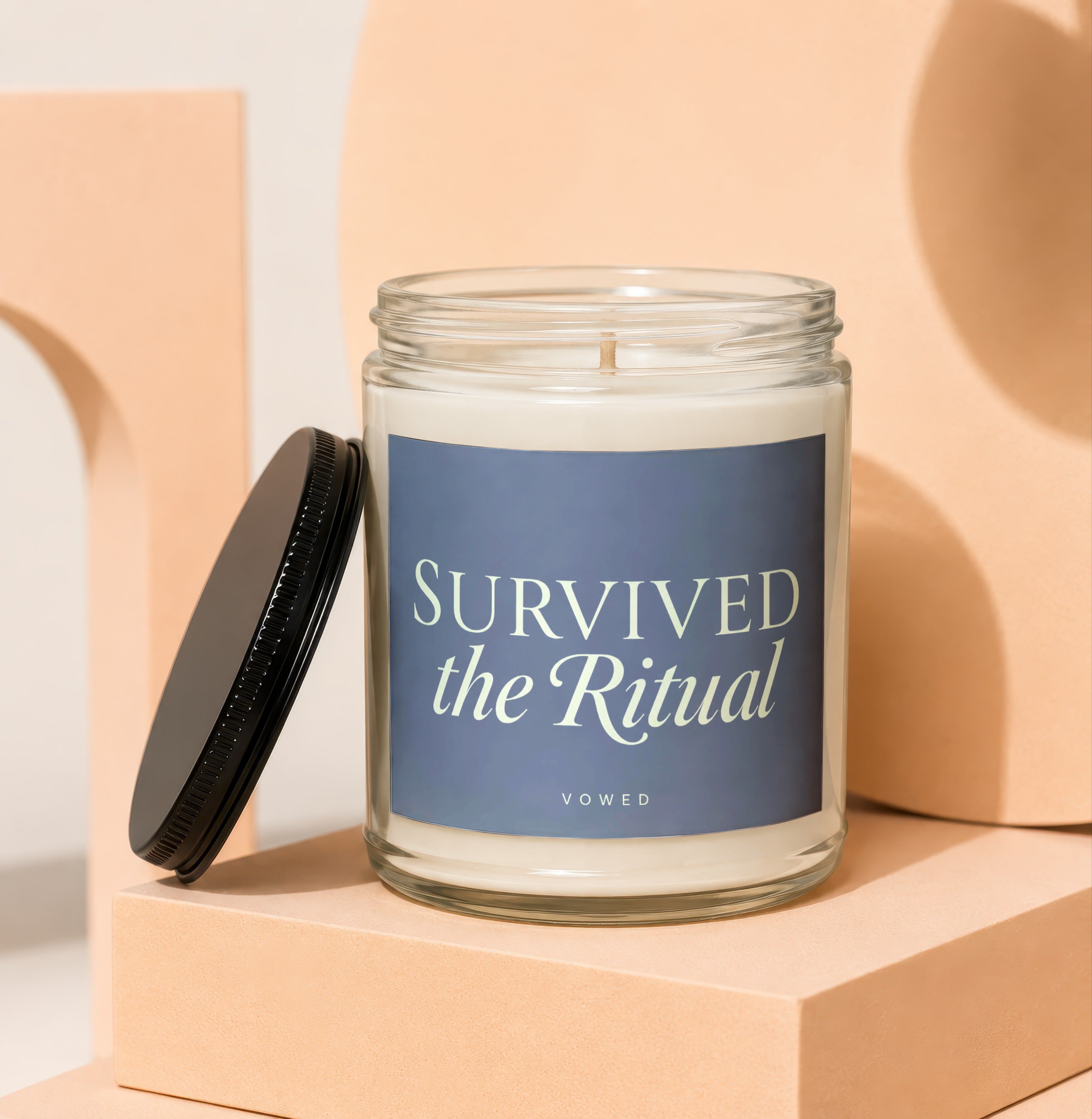 Glass candle with navy label reading "SURVIVED the Ritual" and "VOWED".