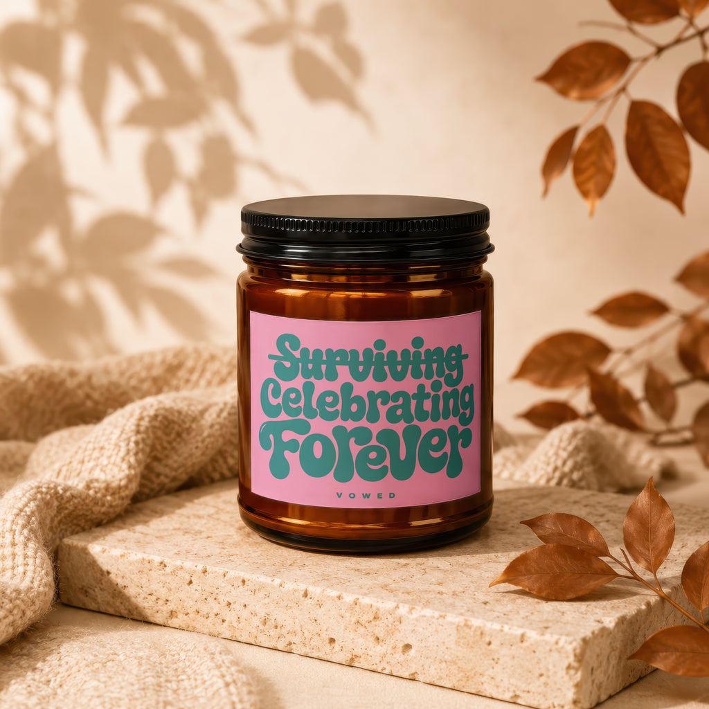Amber candle with pink label reading "Surviving Celebrating Forever" and "Vowed".