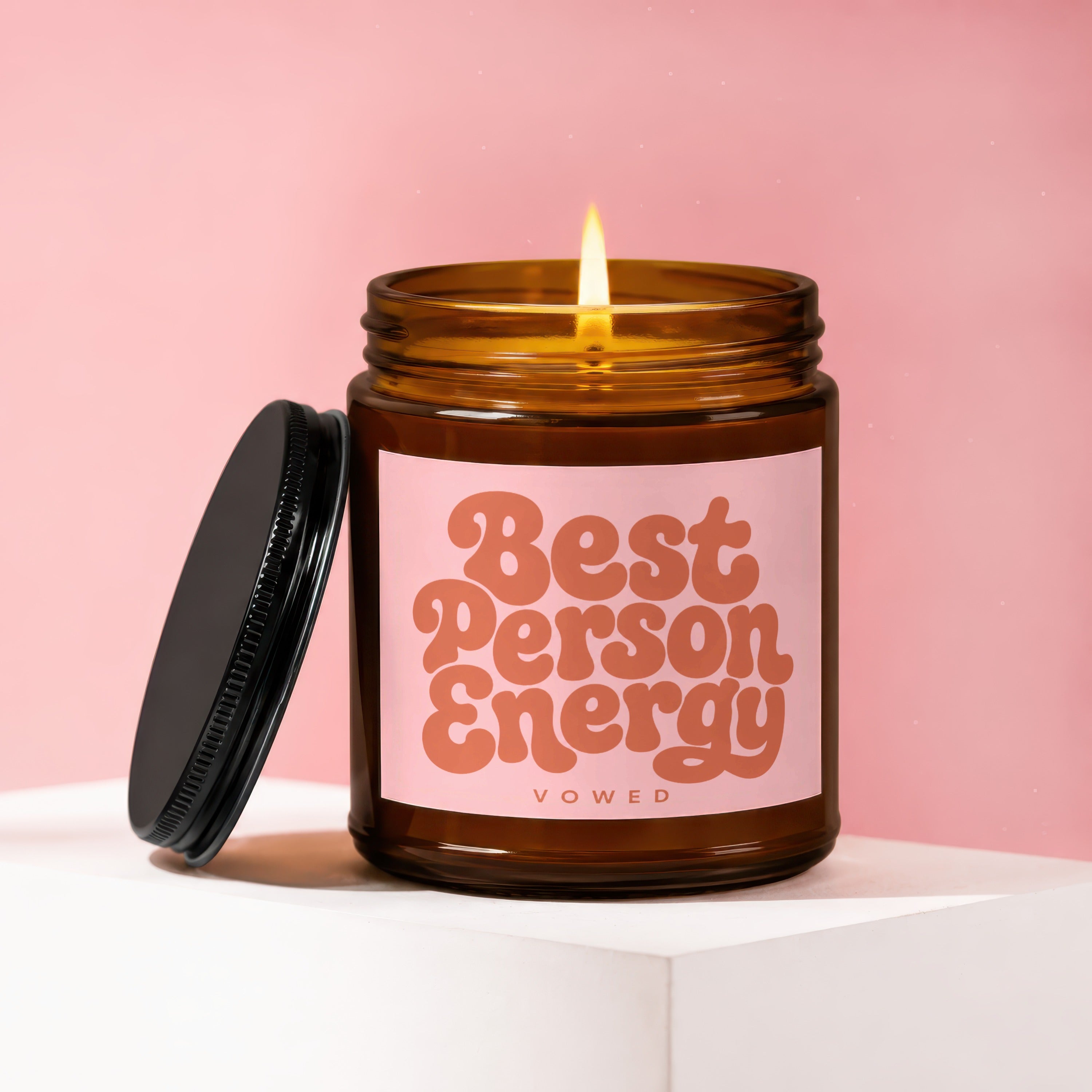 Amber jar candle with lit flame, lid off, labeled "Best Person Energy VOWED".