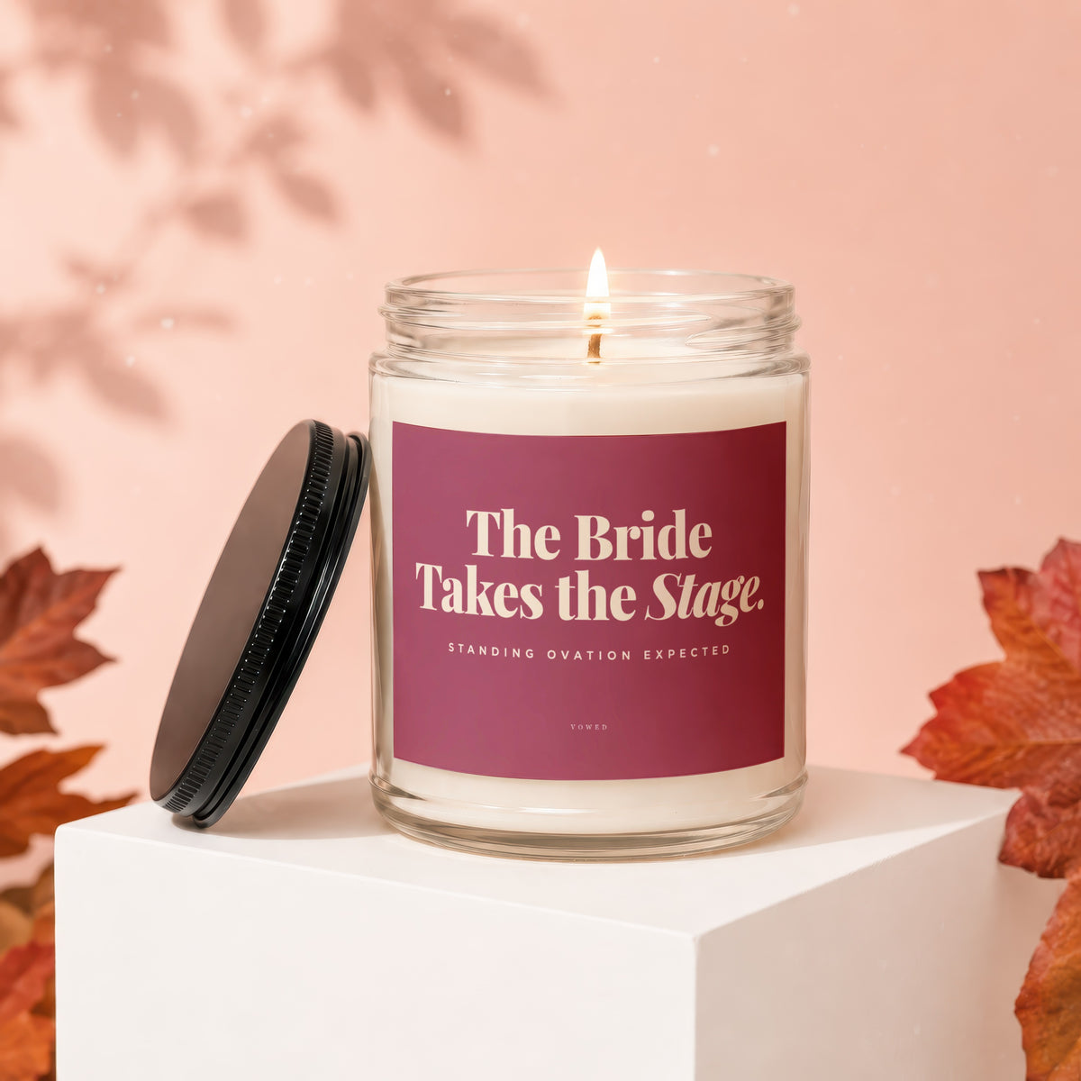 Glass candle with lit wick and label "The Bride Takes the Stage."