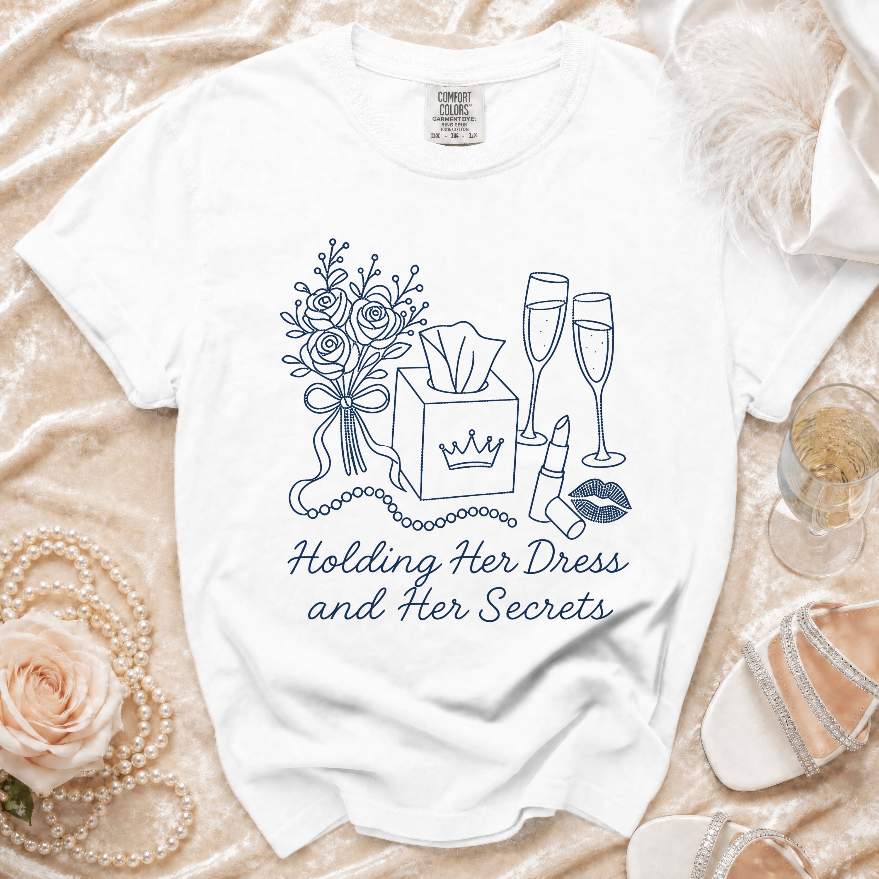 White t-shirt with blue line drawing of flowers, tissue box, champagne glasses, and lipstick, plus text.