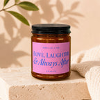 Amber candle with pink label that reads "Smells like Love, Laughter & Always After"