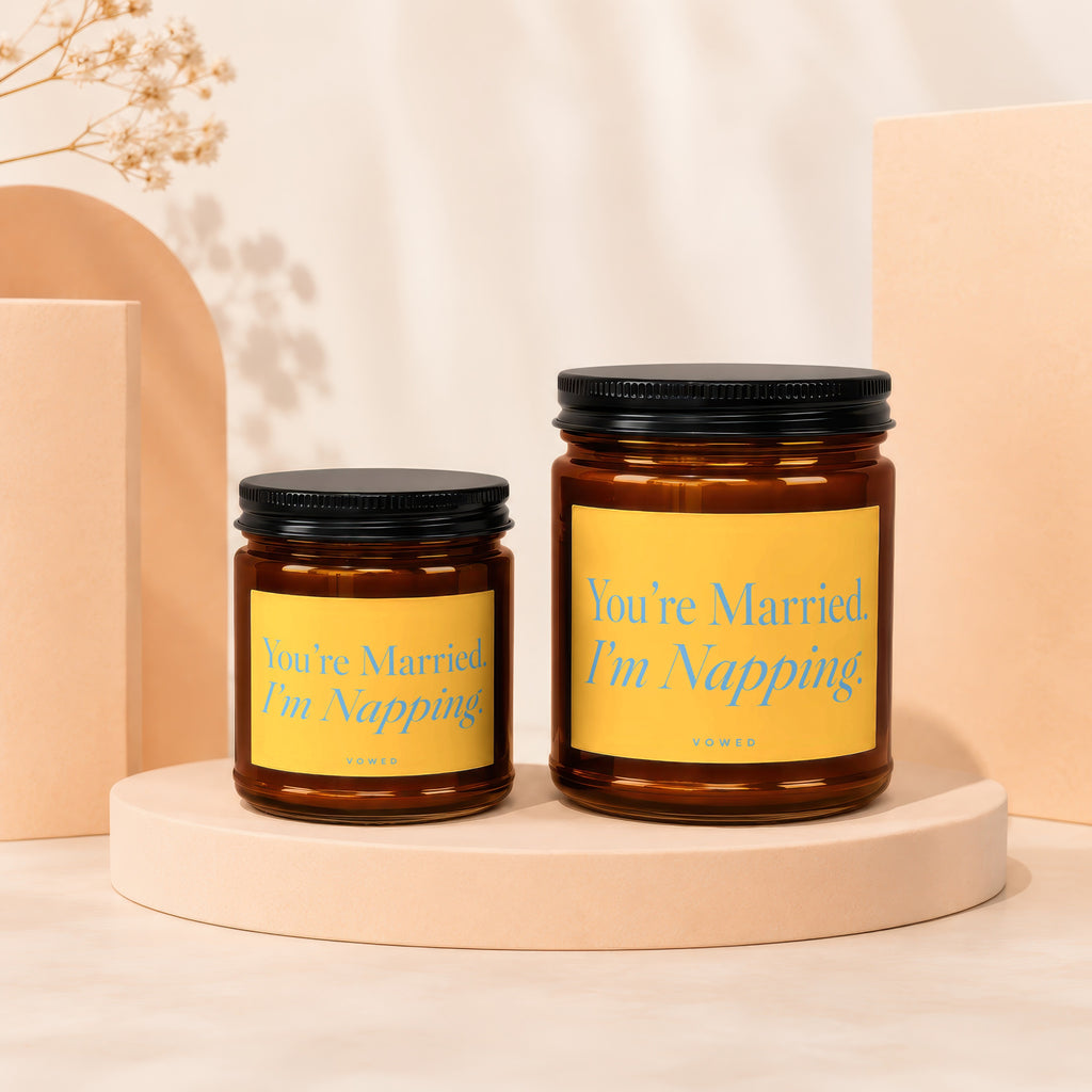 Two amber glass candles with black lids and yellow labels featuring blue text.