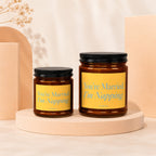 Two amber glass candles with black lids and yellow labels featuring blue text.