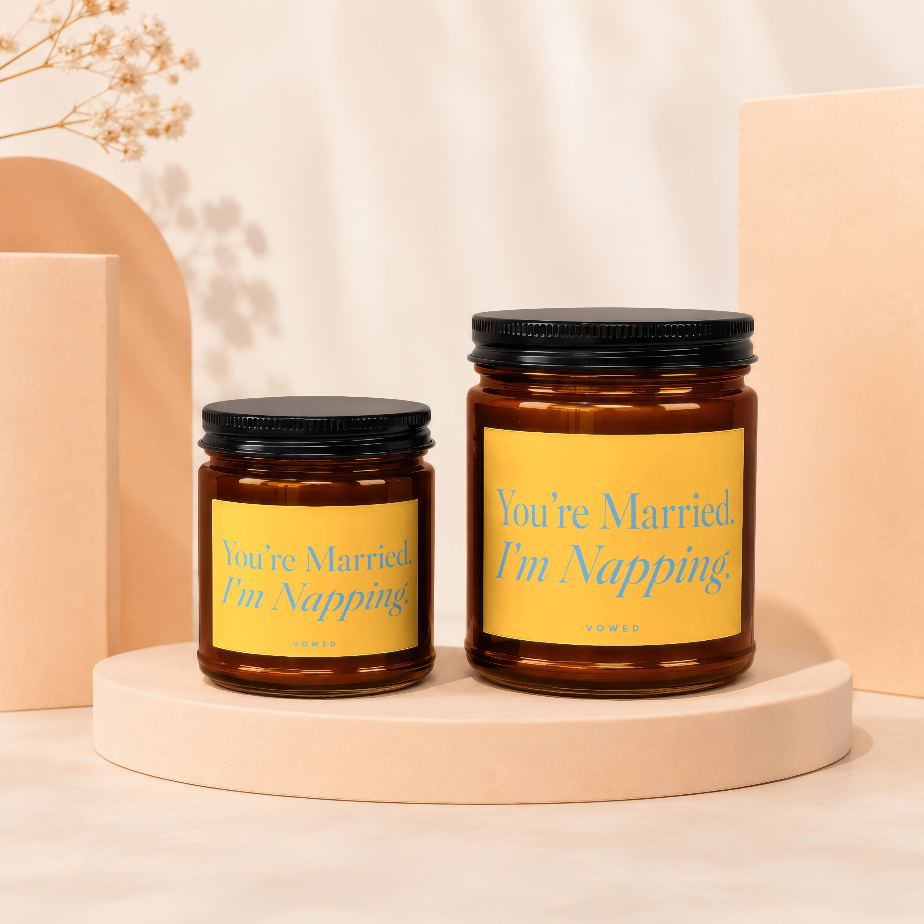 Two amber glass candles with black lids and yellow labels featuring blue text.