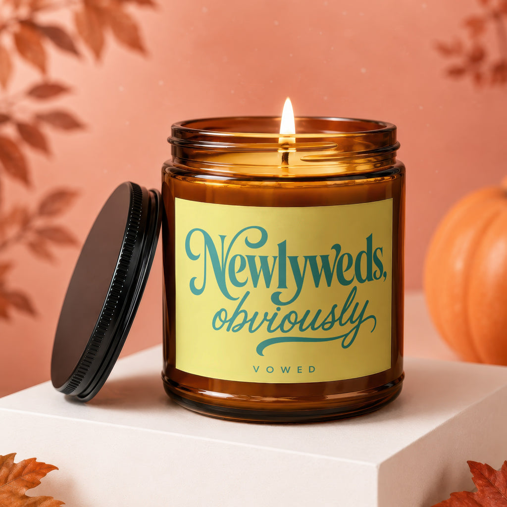 Amber jar candle with lit wick and the text "Newlyweds, obviously VOWED" on a yellow label.