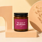 Glass candle with black lid, pink label reads "the man of my dreams."