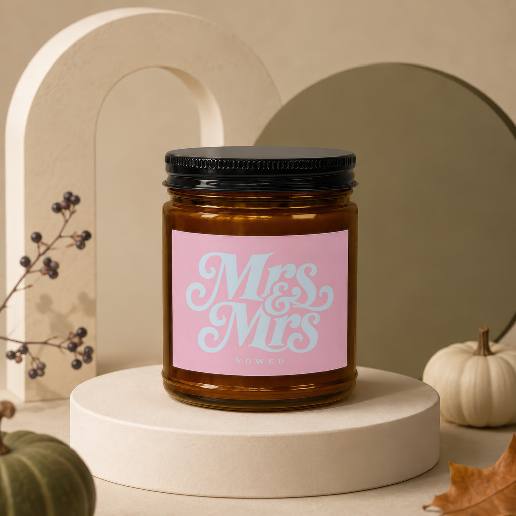 Candle with "Mrs & Mrs VOWED" text on a pink label in a brown glass jar.