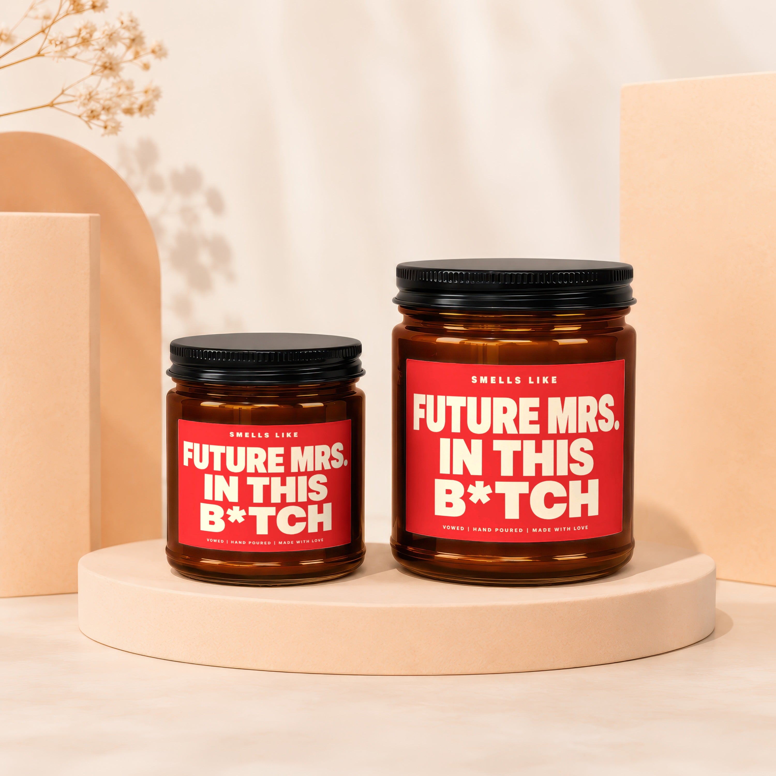 Two amber candles with red labels reading "Smells Like Future Mrs. In This B*tch".