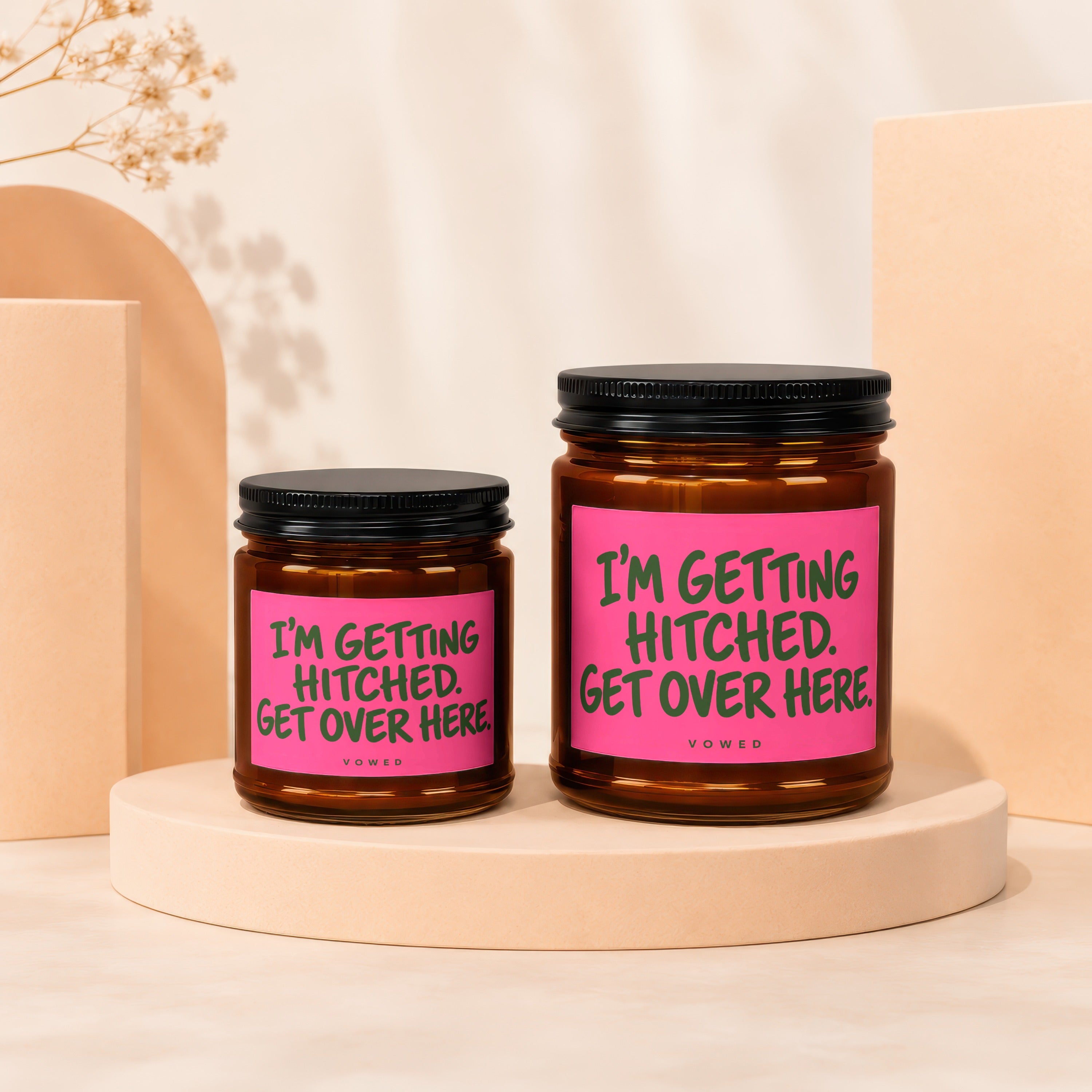 Two amber glass candles with black lids, featuring pink labels with green text.