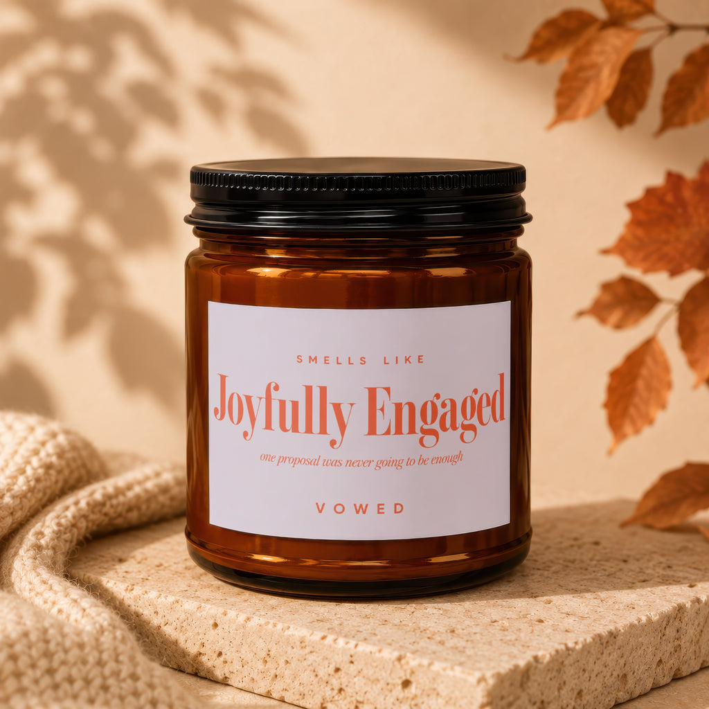 Amber candle in glass jar with "Joyfully Engaged" label on beige background.