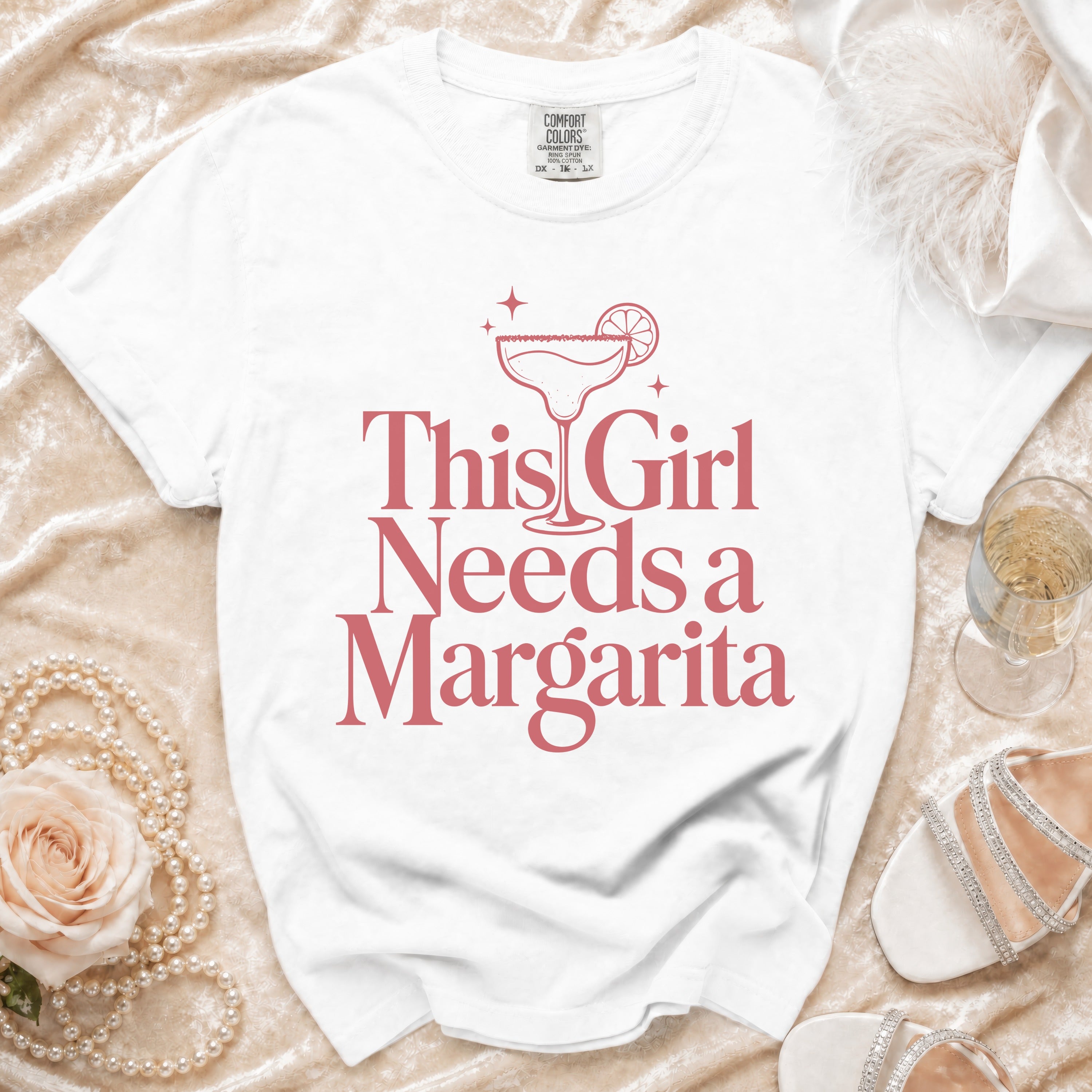 White t-shirt with pink text and margarita graphic that reads "This Girl Needs a Margarita".