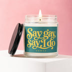 Jar candle with lit wick, featuring a teal label with yellow text "Say gay Say I do VOWED."