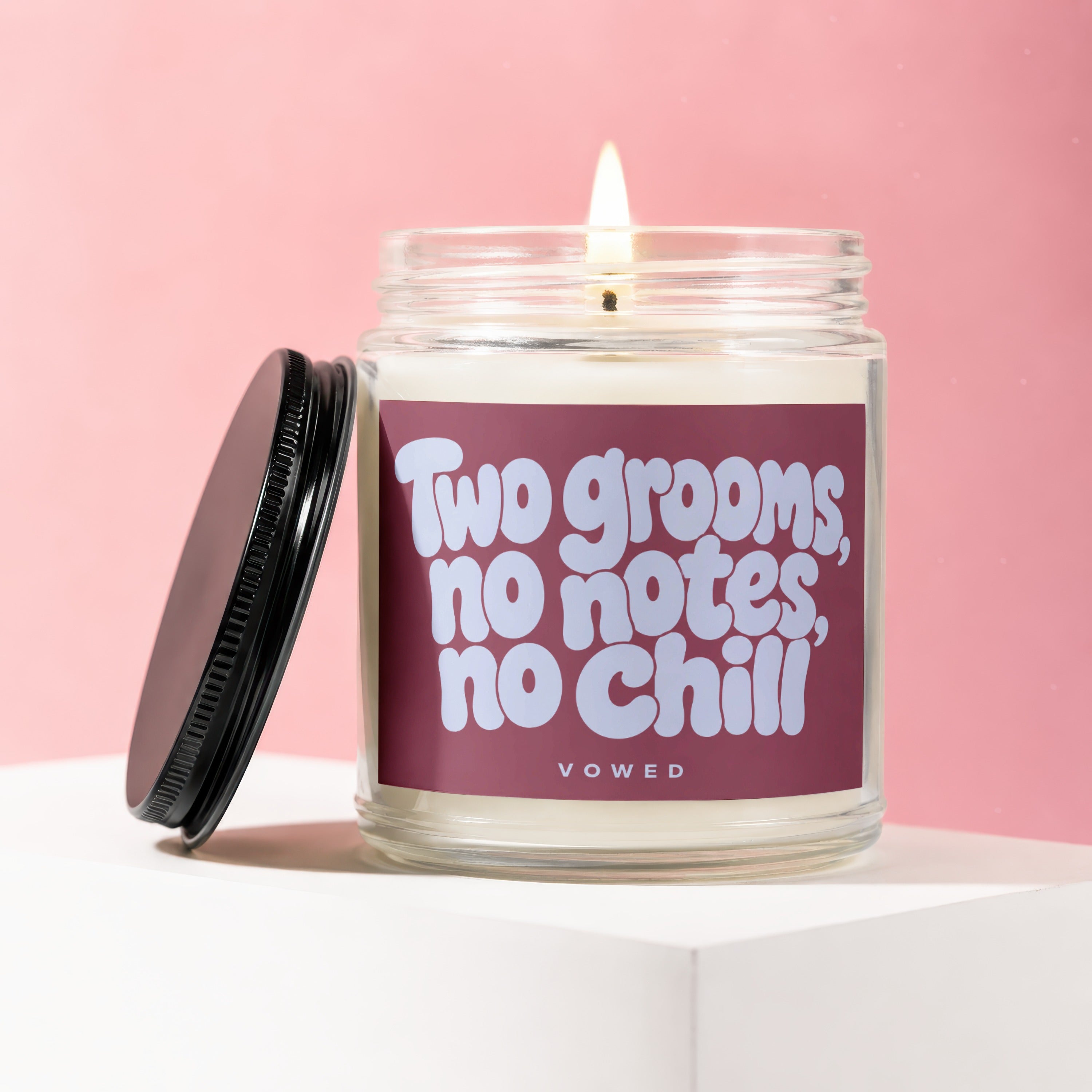 Glass candle with lit flame and label reading "Two grooms, no notes, no chill"