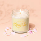 Lit candle in glass jar with "Smells Like Happy Tears" label surrounded by delicate petals.