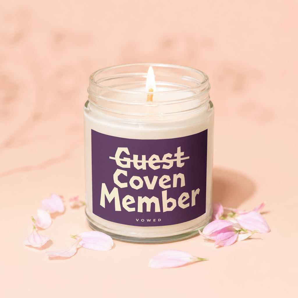 Clear glass jar candle with purple label reading "Guest Coven Member Vowed".