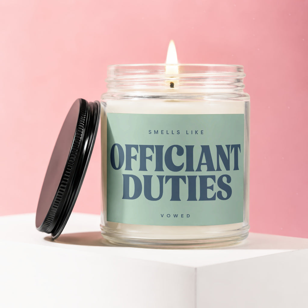 Candle in glass jar with a lit wick, labeled "Smells Like Officiant Duties".