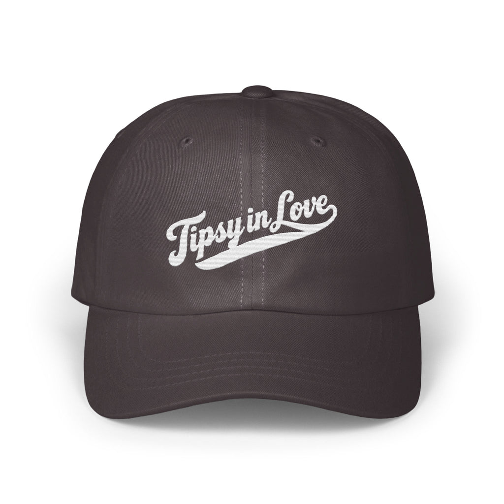 A dark grey baseball cap embroidered with the white script text Tipsy in Love across the front.