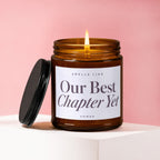 Amber glass candle with lit wick and lid next to it, "Our Best Chapter Yet" text.