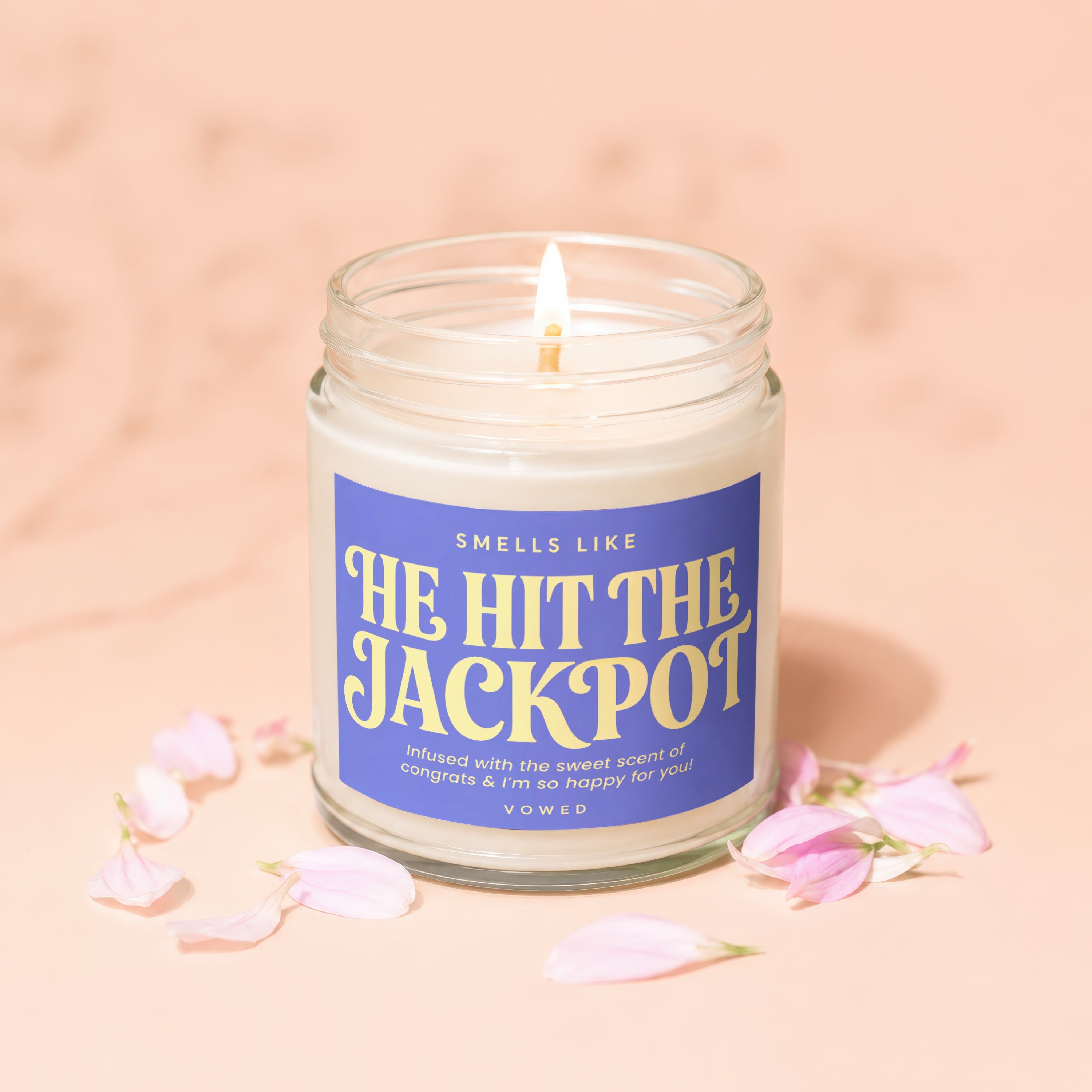 Lit candle in jar, reads "He Hit The Jackpot," surrounded by pink petals.