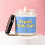 Glass jar candle with lit flame, blue label reads "Equal Parts Love VOWED".