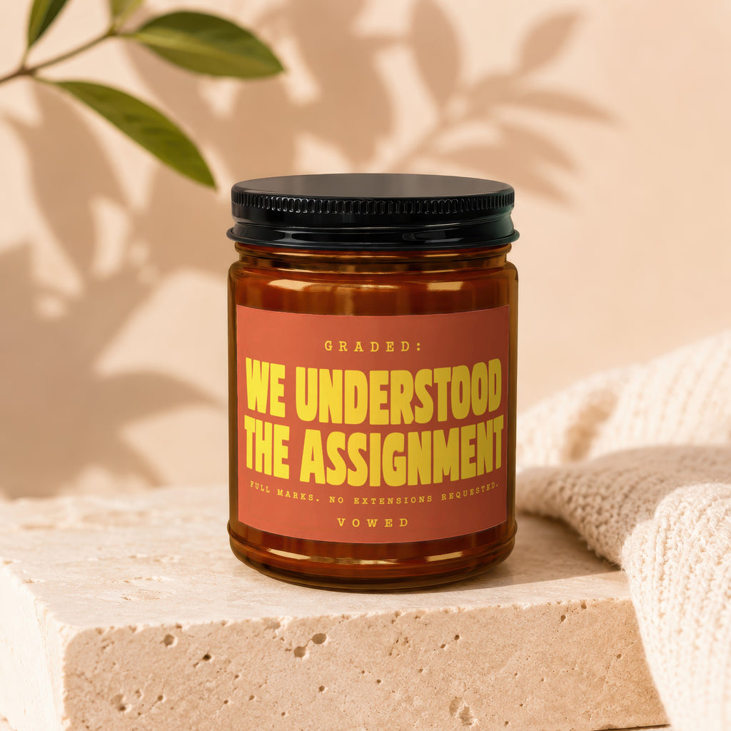 Amber candle labeled "WE UNDERSTOOD THE ASSIGNMENT" with decorative accents.