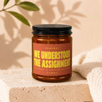 Amber candle labeled "WE UNDERSTOOD THE ASSIGNMENT" with decorative accents.