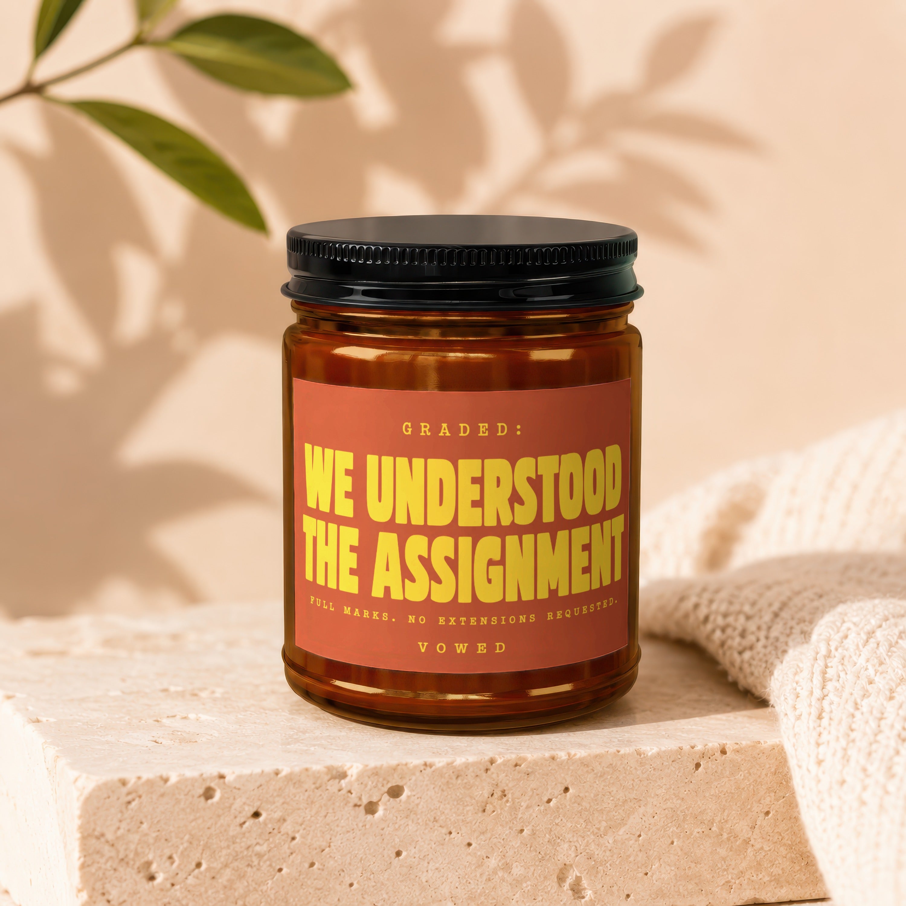 Amber candle labeled "WE UNDERSTOOD THE ASSIGNMENT" with decorative accents.