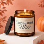 Amber jar candle with lit wick, lid off, reading "Engagement Bliss Vowed".