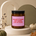 Amber jar candle with pink label reading "CAUTION: WEDDING PLANNING MAY CAUSE LOSS OF SLEEP".