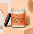 Glass candle with orange label reading "We Registered for This."