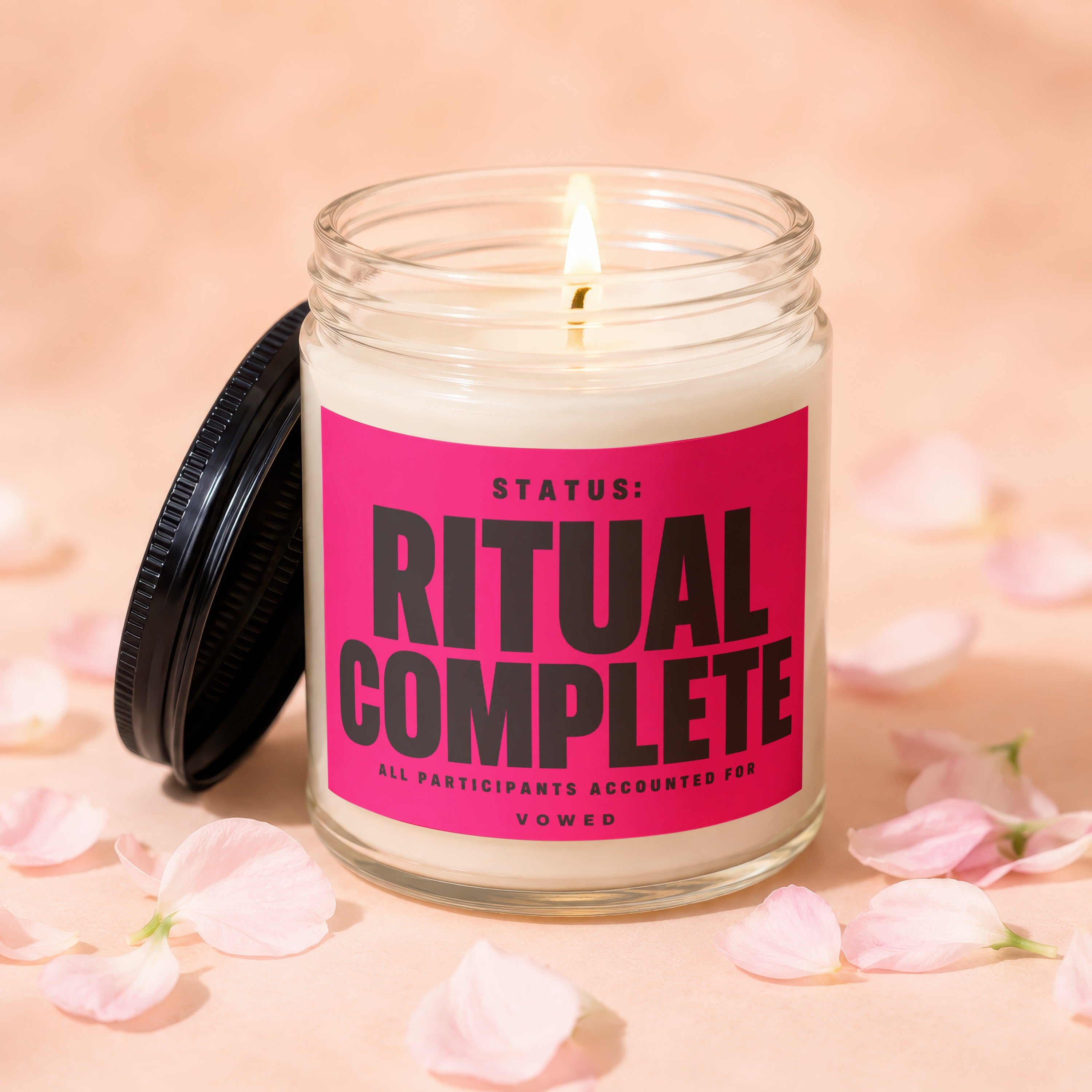 Glass candle with pink label reading "STATUS: RITUAL COMPLETE" surrounded by pink petals.