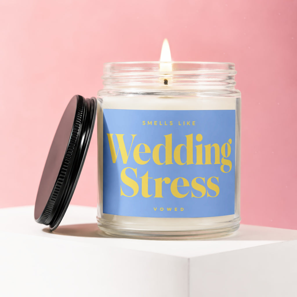 Lit candle in a glass jar with blue label reading "SMELLS LIKE Wedding Stress VOWED"