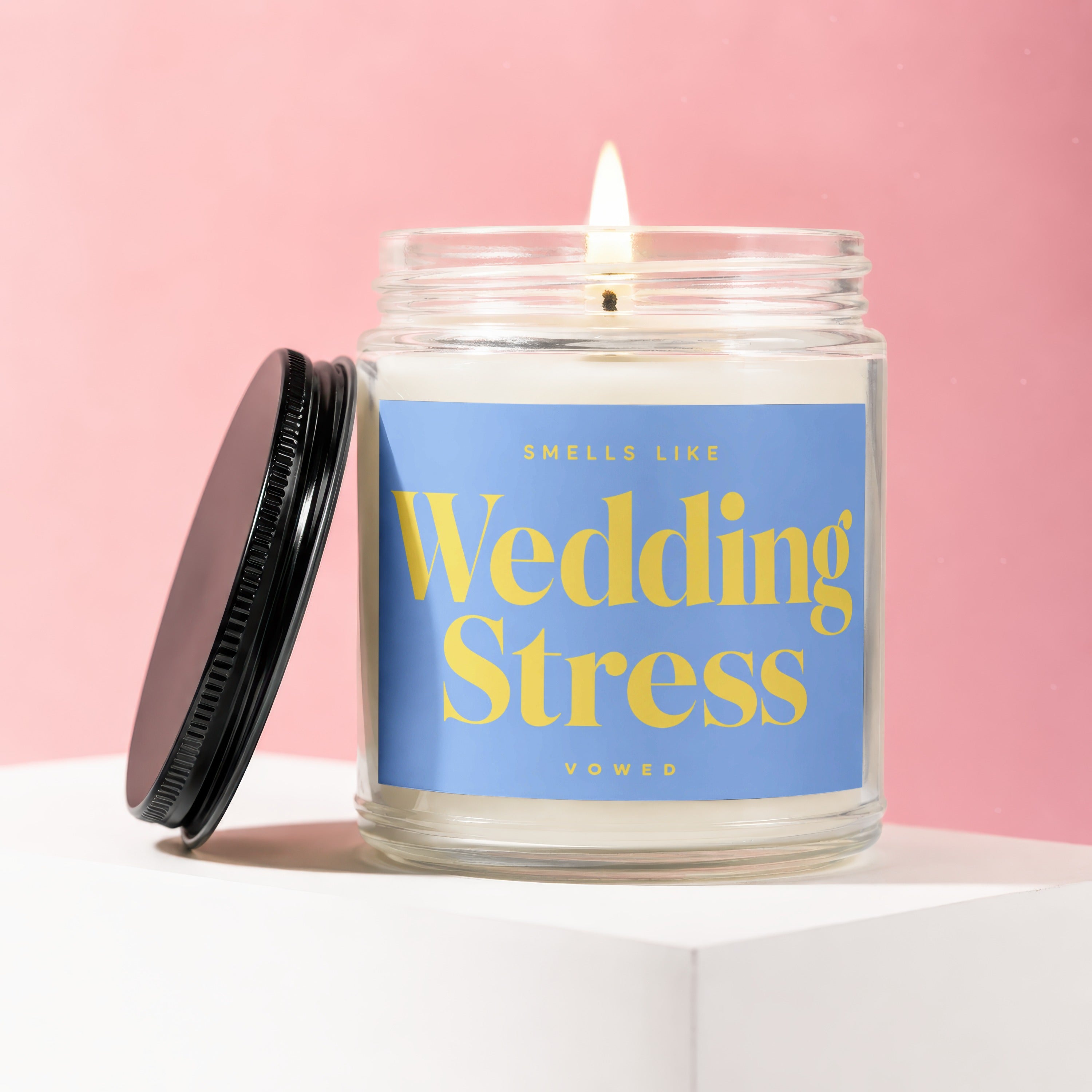 Lit candle in a glass jar with blue label reading "SMELLS LIKE Wedding Stress VOWED"