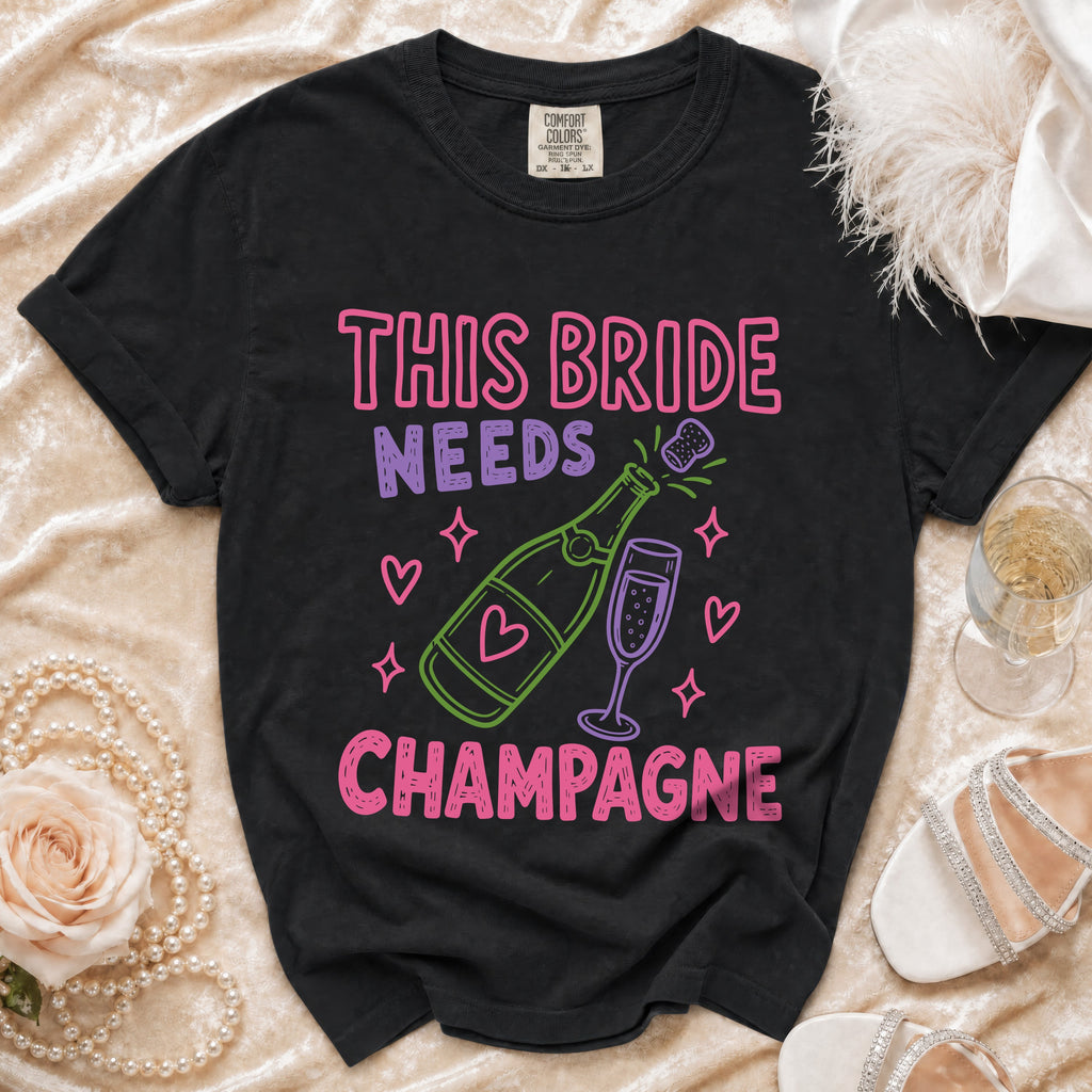 Black t-shirt with "This Bride Needs Champagne" text and champagne bottle graphic.