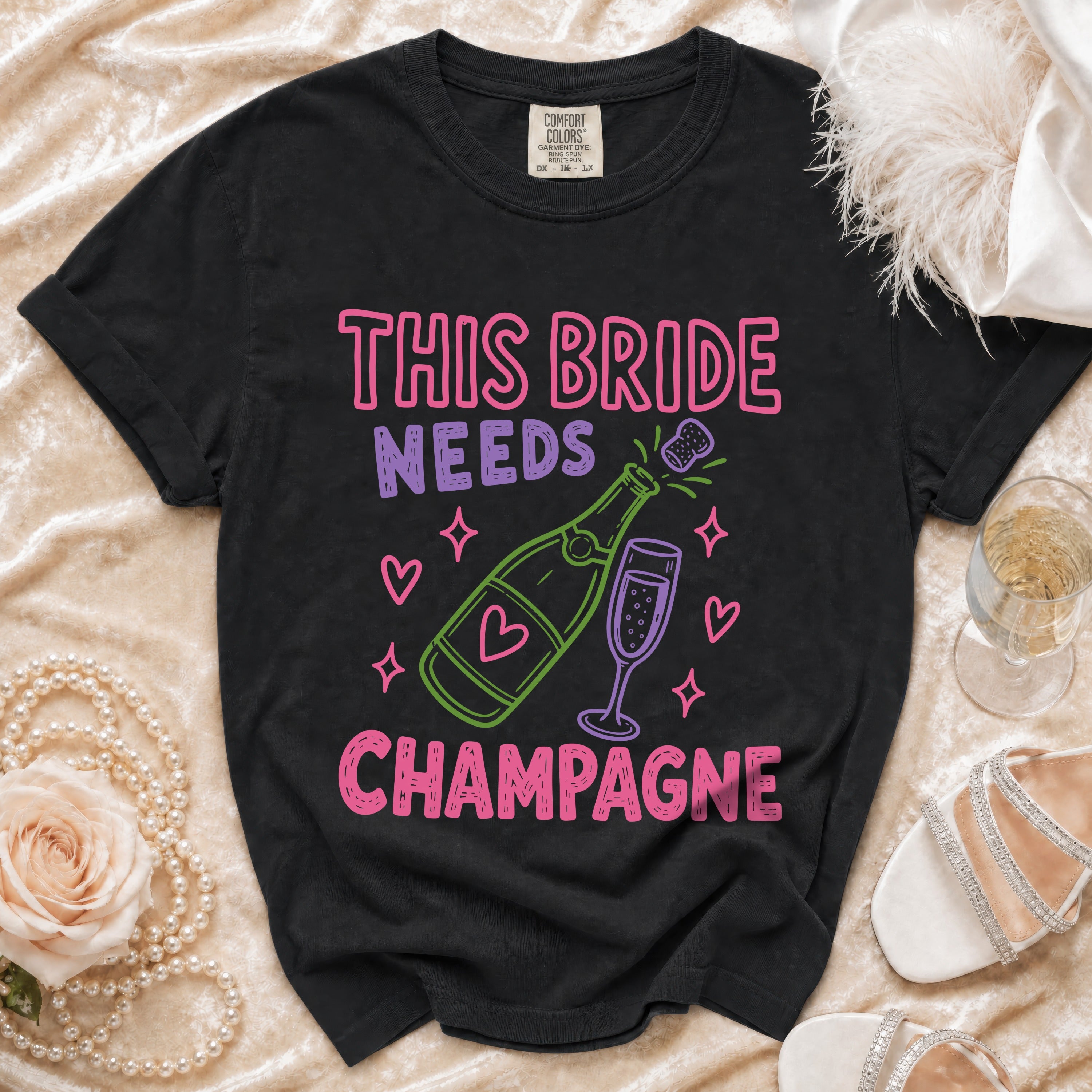 Black t-shirt with "This Bride Needs Champagne" text and champagne bottle graphic.