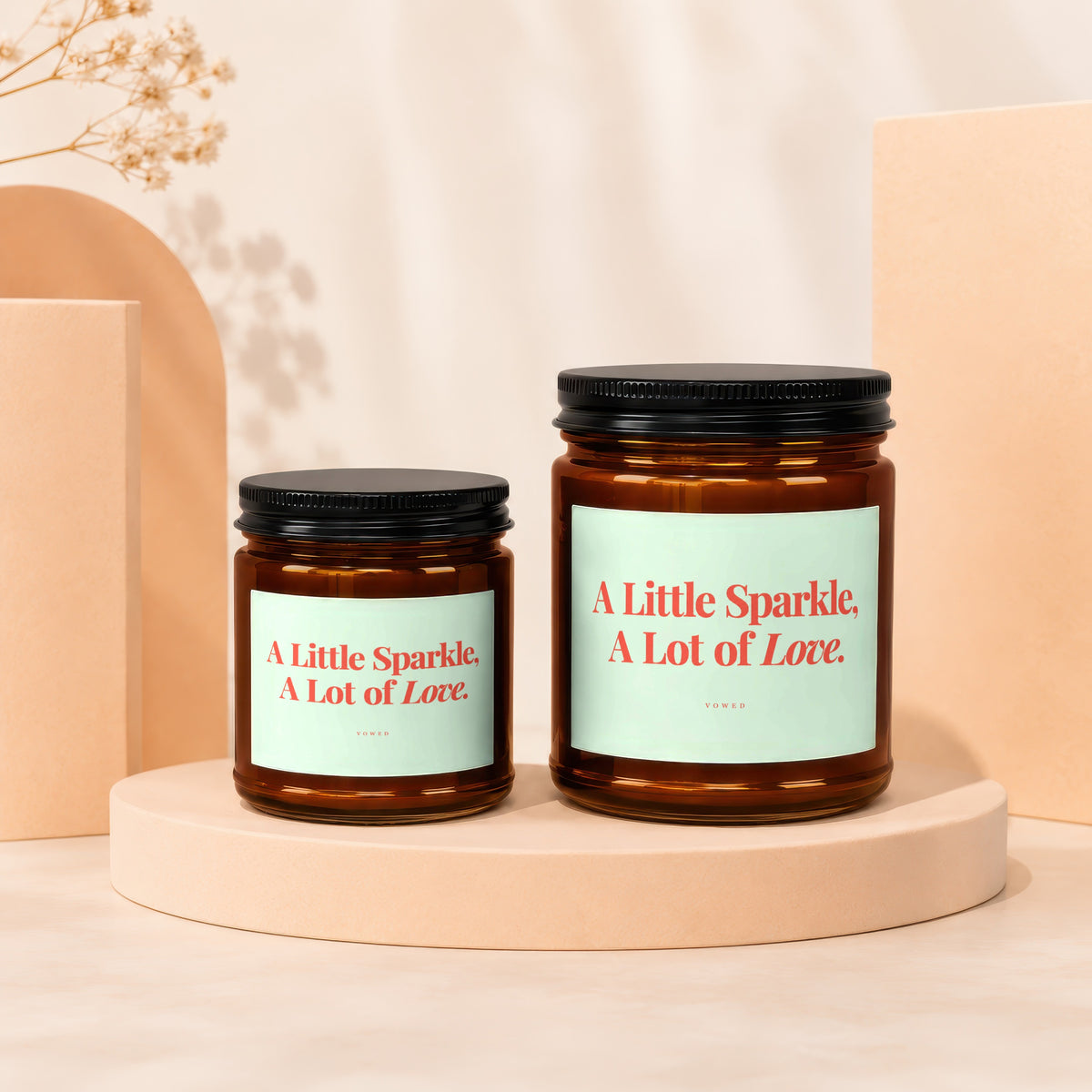Two amber glass candles with black lids, each labeled "A Little Sparkle, A Lot of Love."