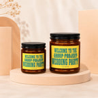Two glass candles with black lids and yellow labels reading "Welcome to the Group Project Wedding Party".