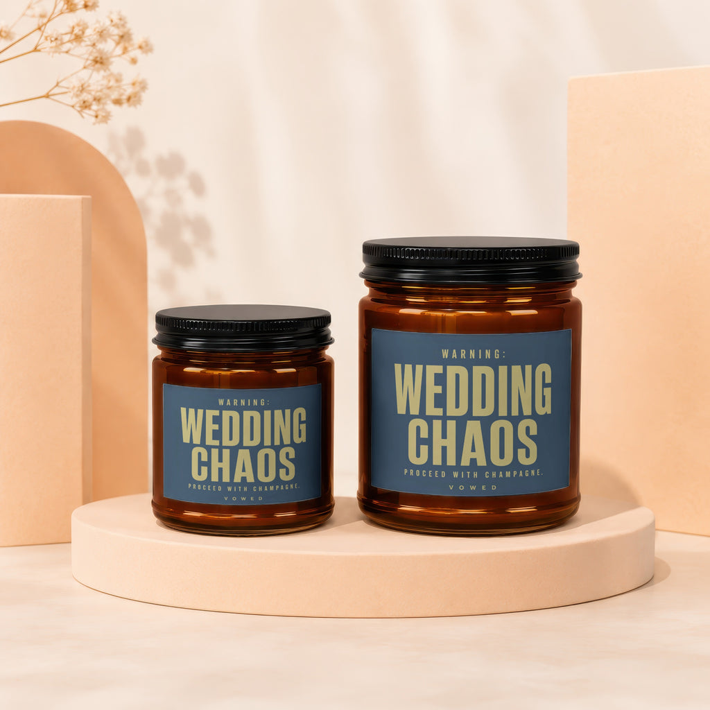 Two amber glass candles with black lids. Labels read "WARNING: WEDDING CHAOS PROCEED WITH CHAMPAGNE. VOWED."