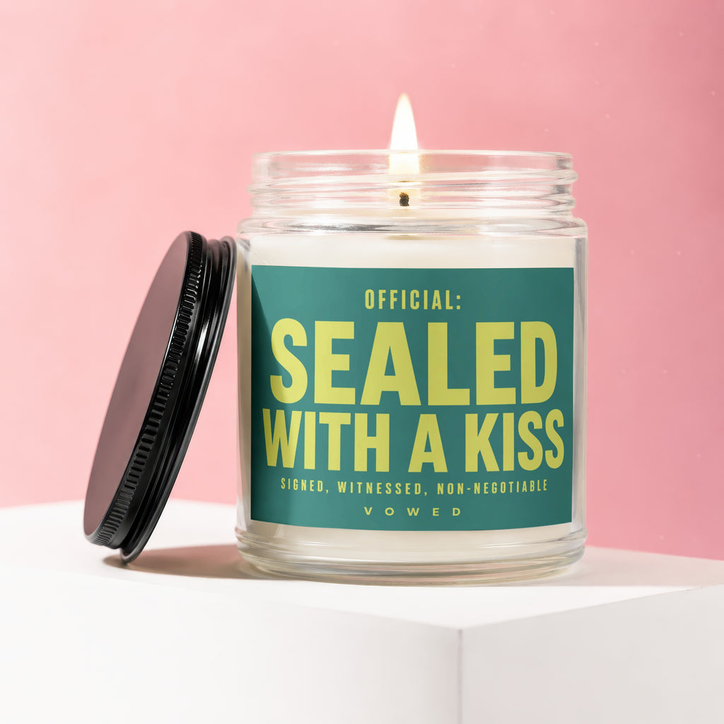 Candle with lit wick and label reading "Official: Sealed With A Kiss."