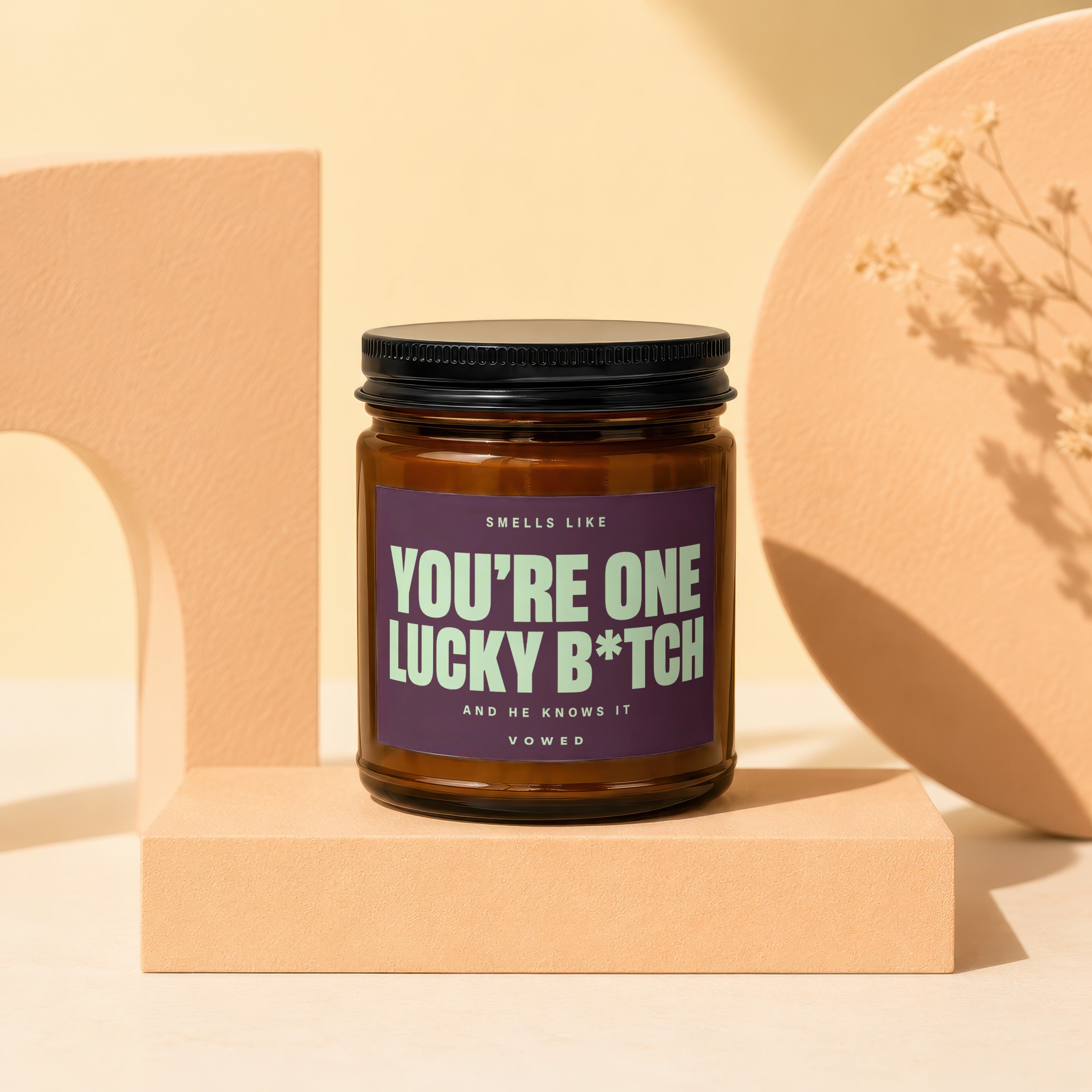 Amber jar candle with purple label reading "You're One Lucky B*tch".